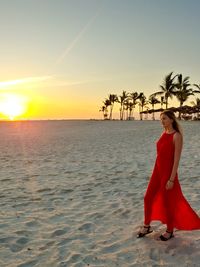 Walking, young woman in red dress on the beach of oman in the sunset.