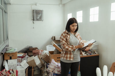 Young woman writing on clipboard standing at home