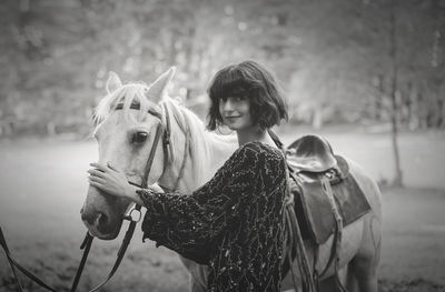 Portrait of young woman standing with horse on field