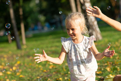 Girl and boy hands catching bubbles against trees