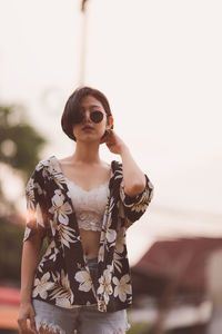 Portrait of young woman wearing sunglasses standing against sky