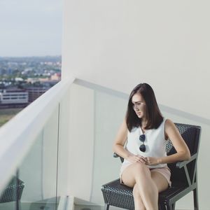 Portrait of woman sitting on chair against railing
