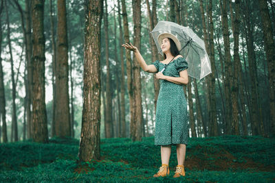 Woman standing by tree trunk in forest