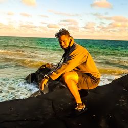 Young man standing on beach against sky during sunset