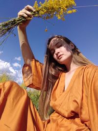 Young woman smiling while holding plant against sky