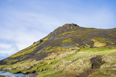 Majestic mountain by geothermal stream in reykjadalur valley against blue sky