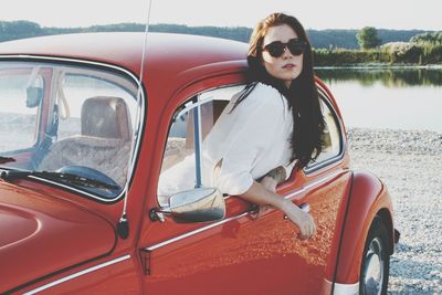 Portrait of woman sitting in red vintage car at lakeshore