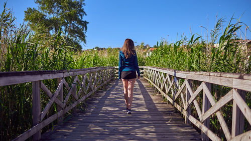 Rear view of woman on footbridge against sky