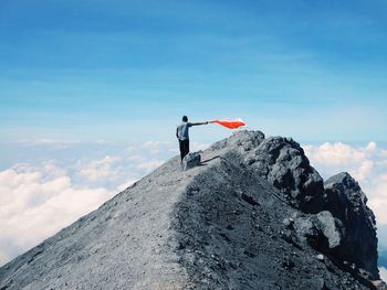 Low angle view of man holding flag while standing rocky mountains sky during sunny day