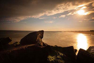 Rock formations on beach against cloudy sky at sunrise