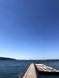 Pier over sea against clear blue sky