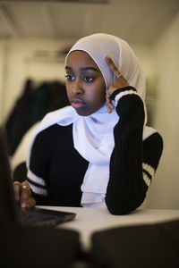 Thoughtful girl wearing scarf using laptop in classroom