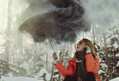 Woman looking at smoke in umbrella during winter