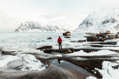 Man standing on snowcapped mountain by sea against sky