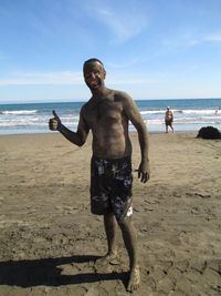 Portrait of smiling man covered in sand showing thumps up on beach