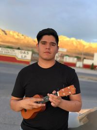 Young man playing guitar against sky