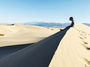 Man on sand dune in desert against sky