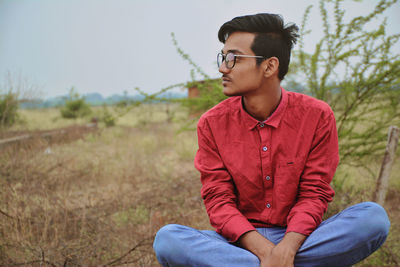 Thoughtful young man looking away while sitting on field