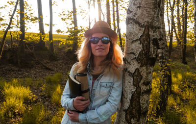 Young woman standing by tree trunk in forest