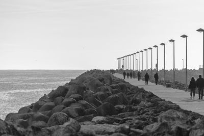 People on rocks by sea against clear sky