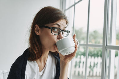 Portrait of young woman drinking coffee by window