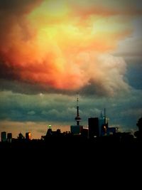 Silhouette of city against cloudy sky during sunset