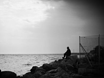 Rear view of woman sitting on rock at seaside