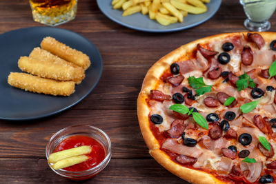 Pizza on a platter close-up on the table with ketchup, juice, sauce and potatoes on a  wooden table.