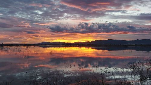 Scenic view of lake against dramatic sky during sunset