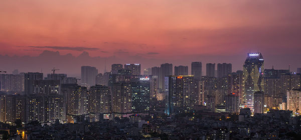 Illuminated buildings in city against sky during sunset