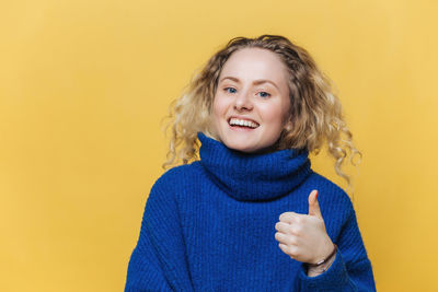 Portrait of young woman standing against yellow background