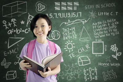 Portrait of girl standing against blackboard