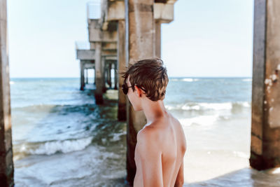 Rear view of shirtless boy on beach