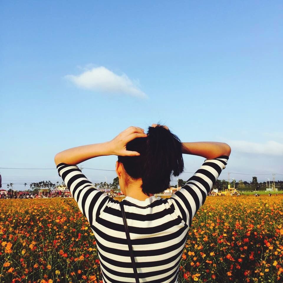 leisure activity, lifestyles, rear view, waist up, flower, standing, casual clothing, field, sky, sunlight, beauty in nature, nature, freshness, holding, growth, person, rural scene, long hair, cloud - sky, sunny, agriculture, outdoors, multi colored, scenics, day, tranquility, summer, sea, farm, carefree