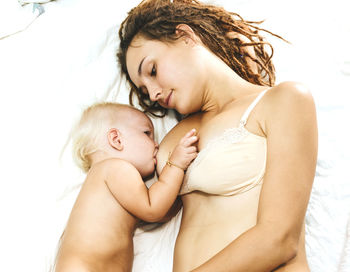 High angle view of mother breastfeeding daughter on bed at home