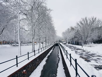 Snow covered road by canal against sky