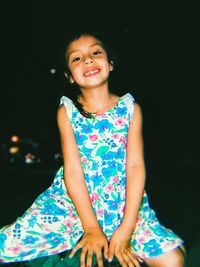 Portrait of smiling girl sitting against black background