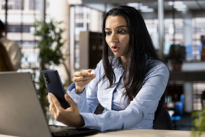 Young woman using phone while sitting at cafe