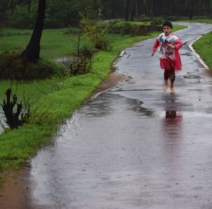 Full length of boy running on wet country road in the rain