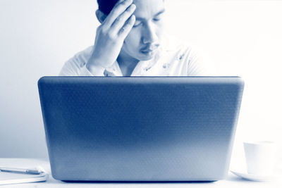 Man with head in hands looking at laptop against wall