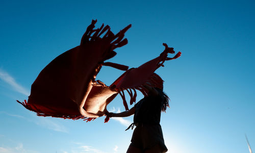 Low angle view of woman holding scarf while standing against blue sky