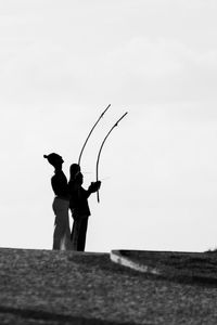 Silhouette man fishing at sea against clear sky