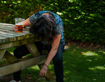 Woman having beer while sitting at table in yard