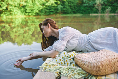Side view of young woman sitting by lake