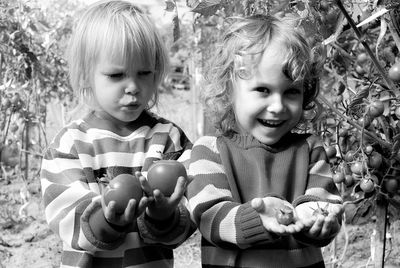 Happy boy with shocked brother holding tomatoes in organic farm