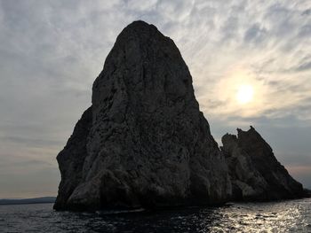 Rock formation in sea against sky during sunset