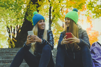 Two girls sitting in the park using smartphone. teen using mobile phone. sisters chat with friends.