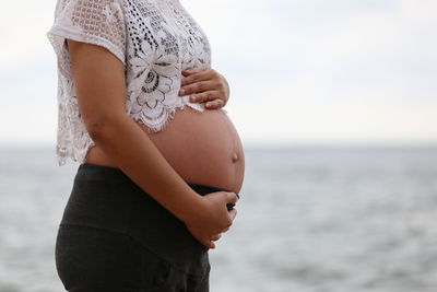 Midsection of woman standing by sea against sky