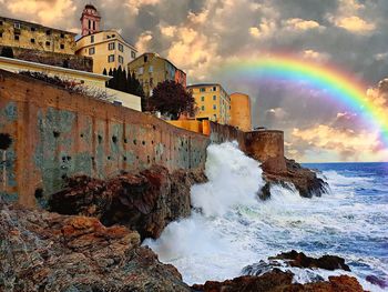 Rainbow over sea and buildings against sky