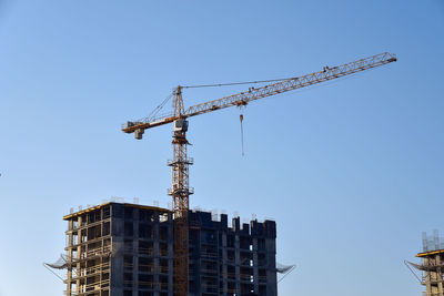 Low angle view of crane by building against clear blue sky